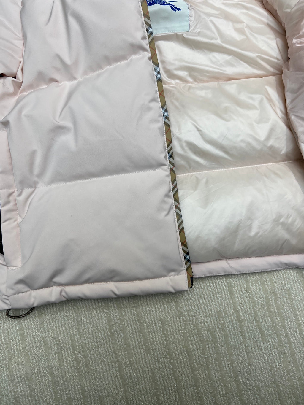 Long puffer jacket close-up of quilted padding and front zipper edge, light pink.