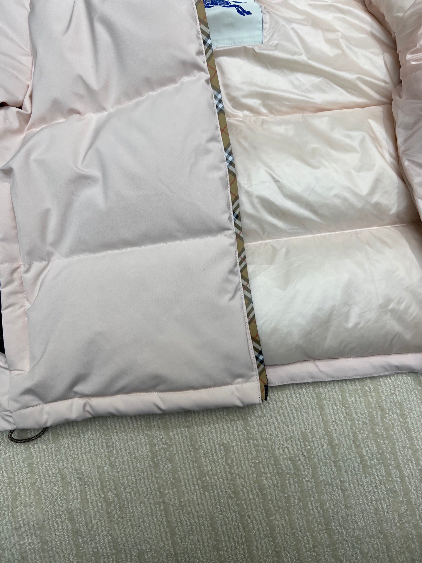 Long puffer jacket close-up of quilted padding and front zipper edge, light pink.
