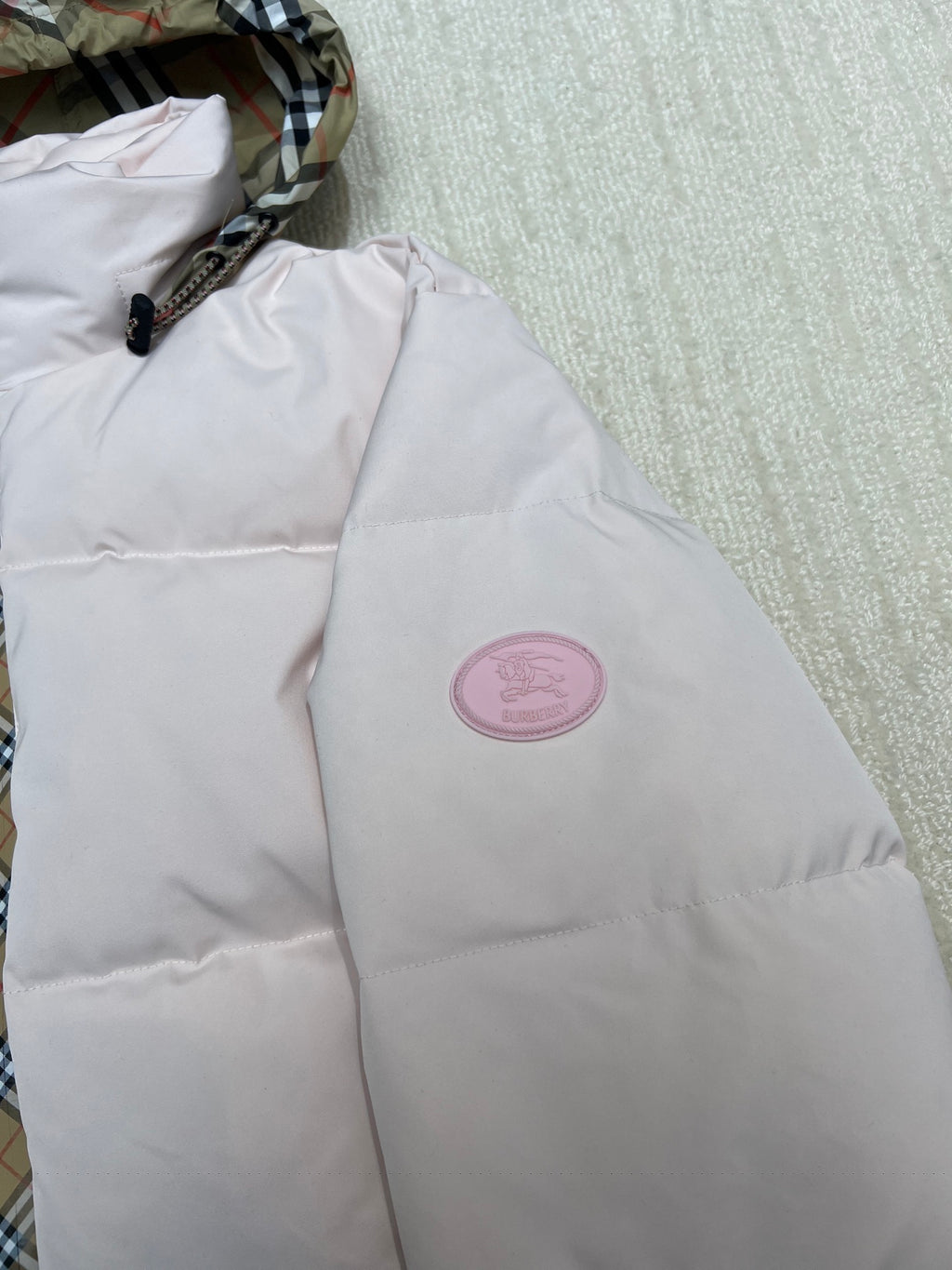 Light pink long puffer jacket with round logo patch on chest.