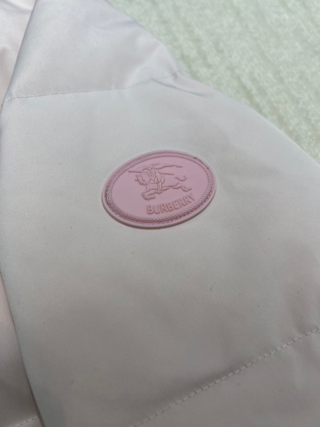 Round pink logo patch on light pink puffer jacket fabric.