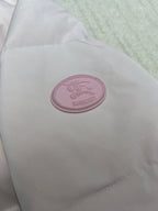 Round pink logo patch on light pink puffer jacket fabric.