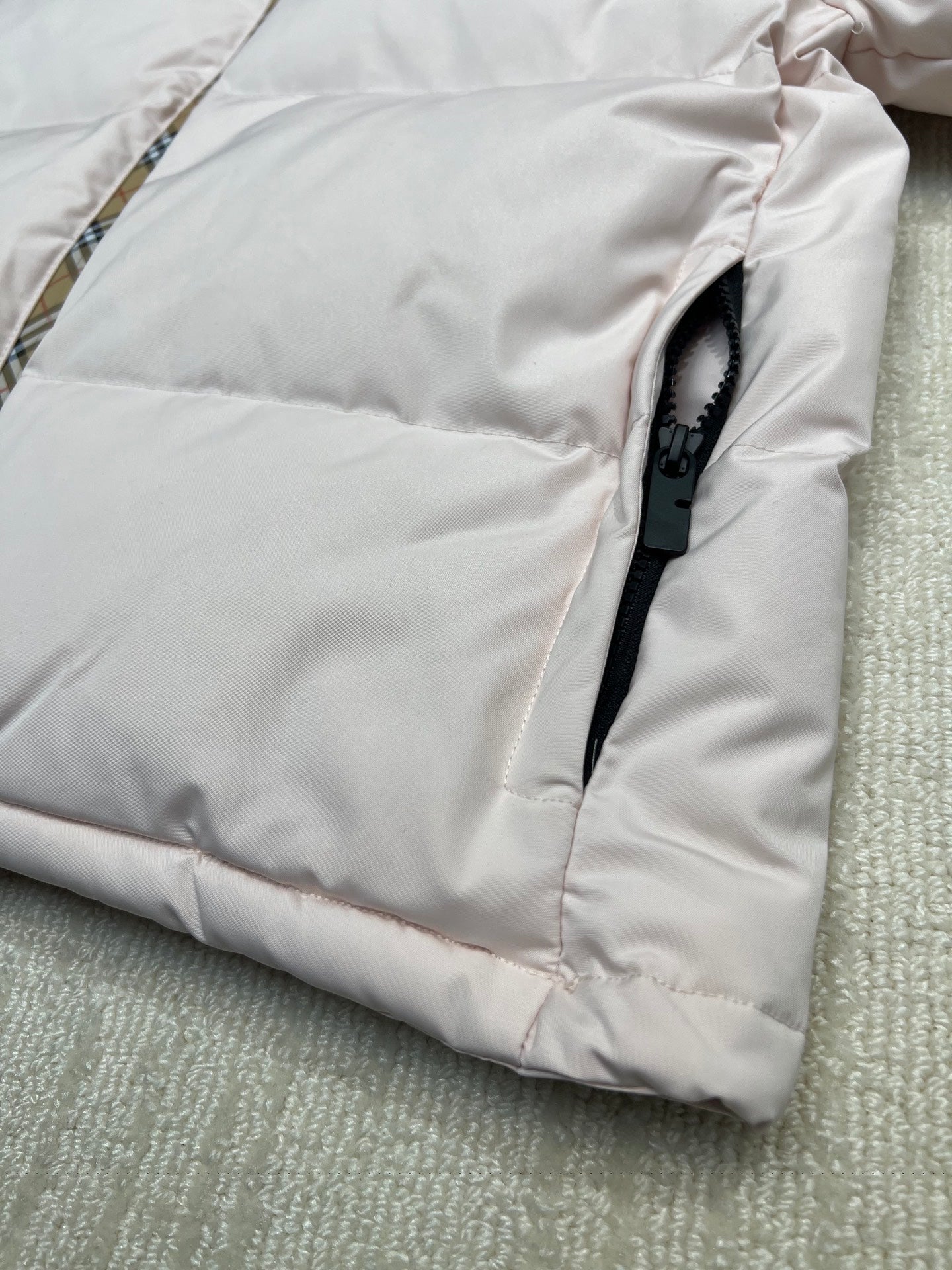 Light pink long puffer jacket with zip pull tab and stitched paneling.