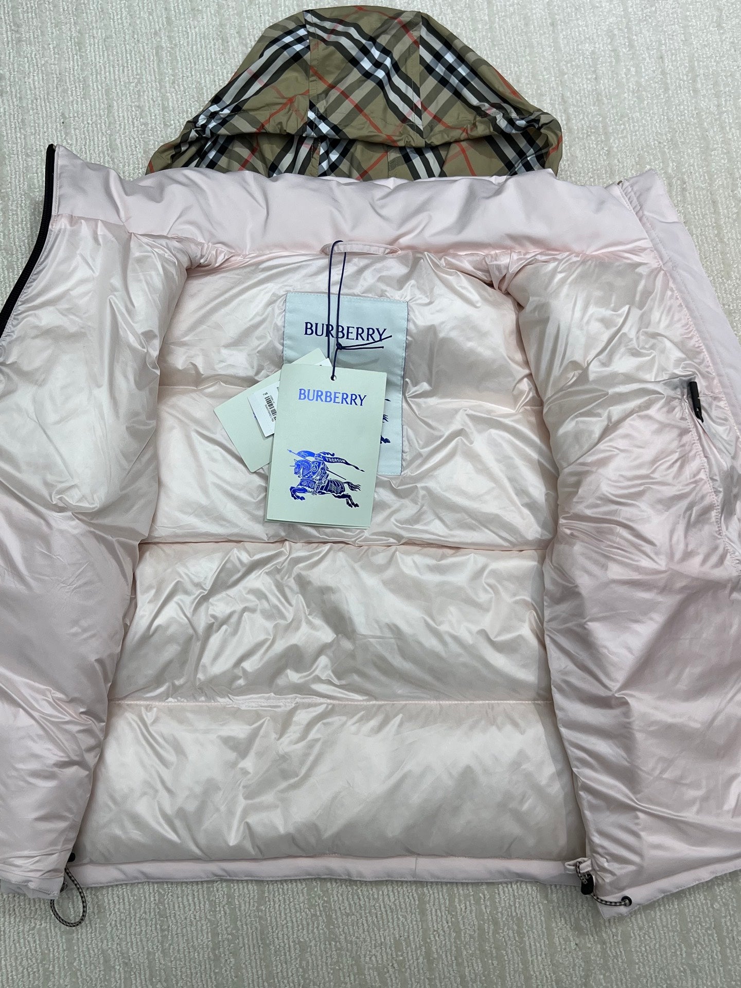 Light pink long puffer jacket laid flat, hood folded, neck label visible.