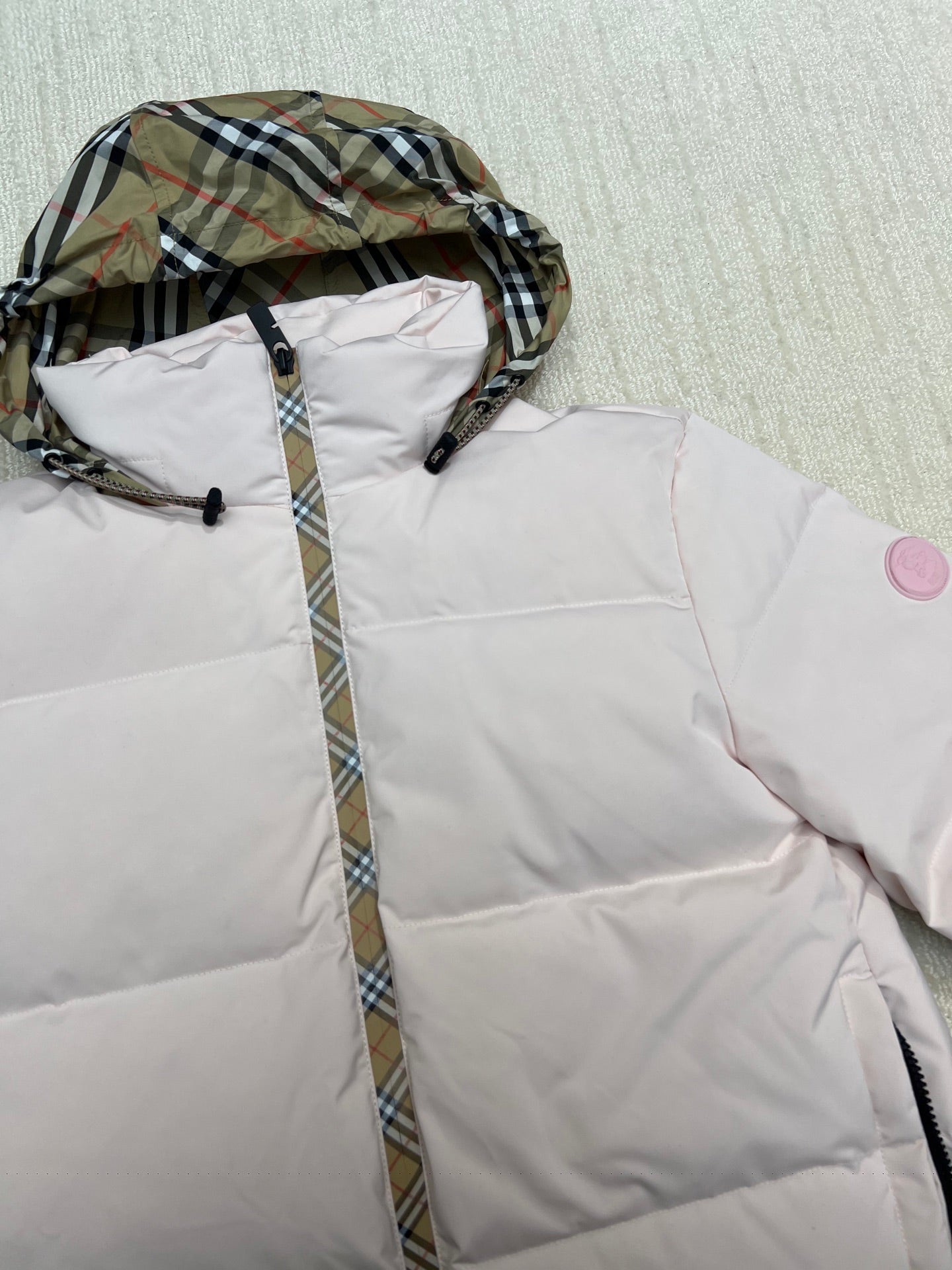Hooded long puffer jacket detail: plaid hood lining on light pink body.