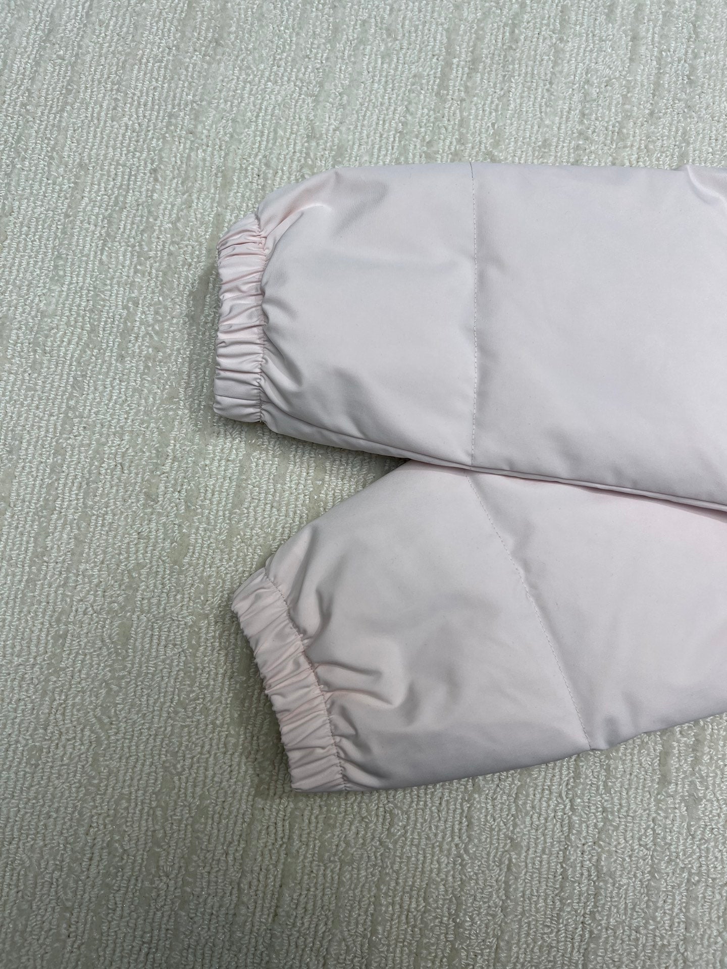 Light pink puffer jacket sleeves and cuff area laid flat, padded construction.