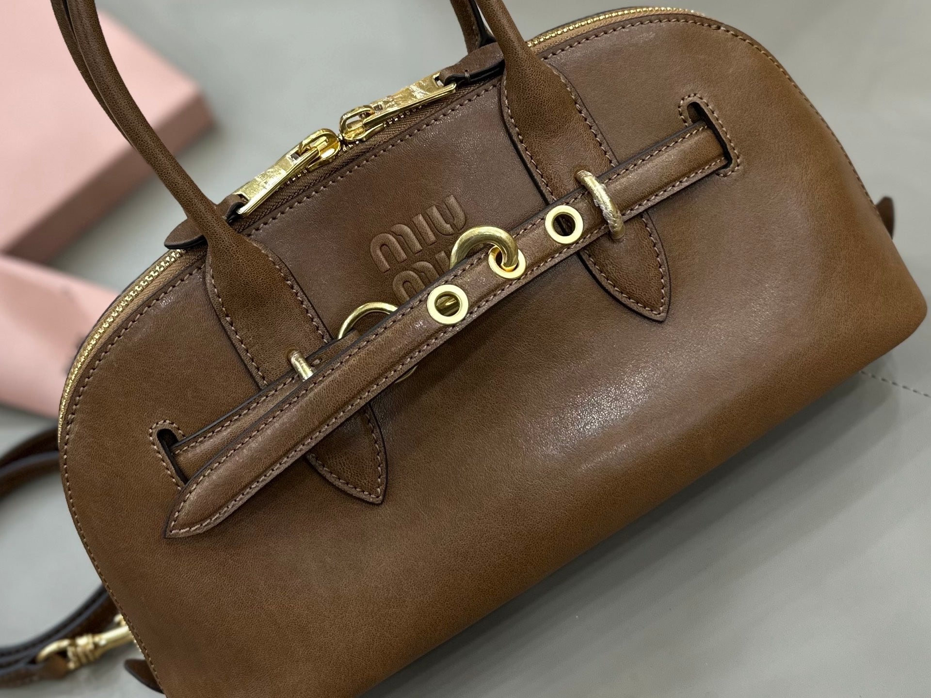 MiuMiu brown leather handbag front detail with logo, grommets, and gold hardware