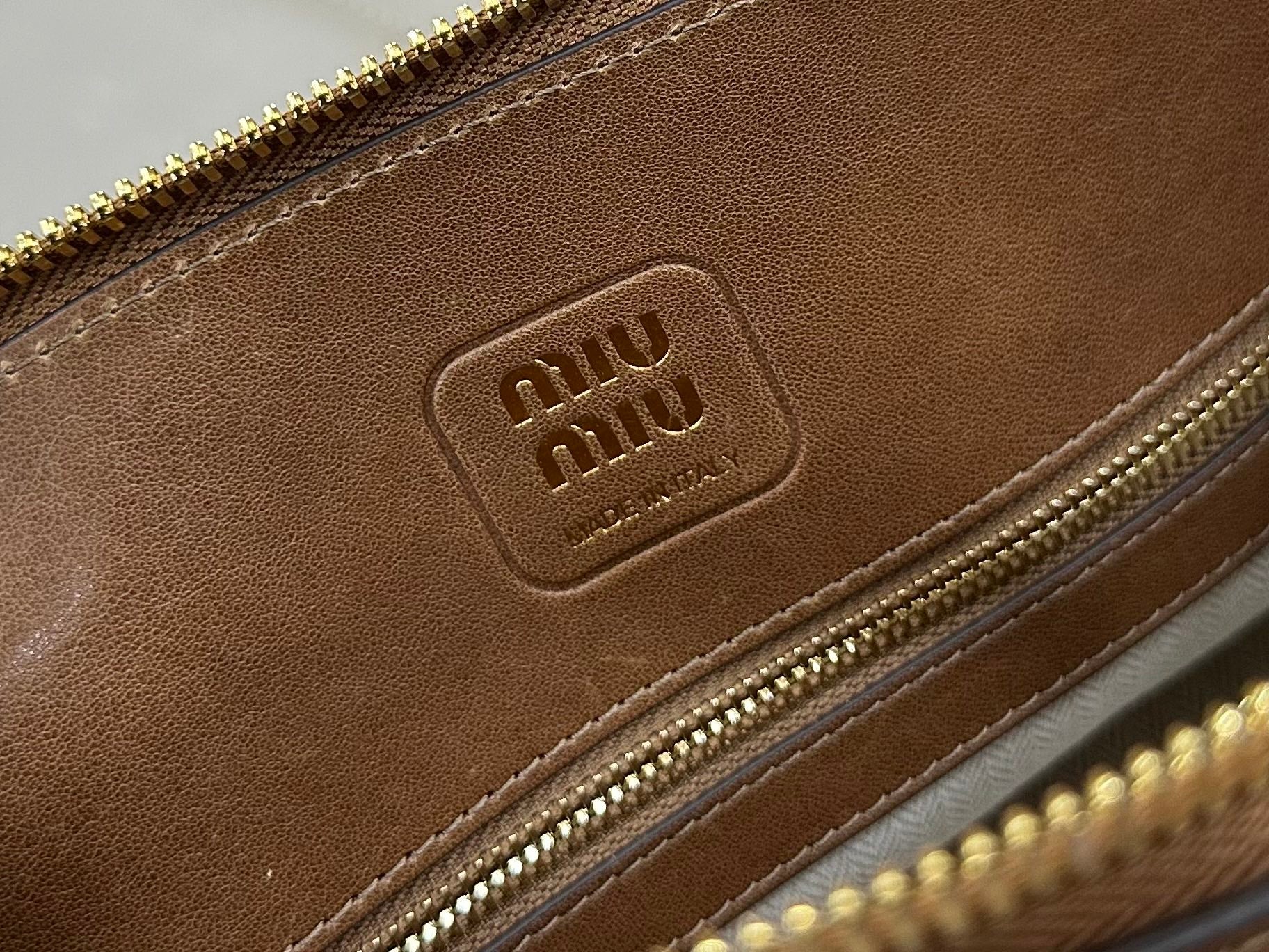 MiuMiu brown leather handbag closeup of embossed logo on front panel