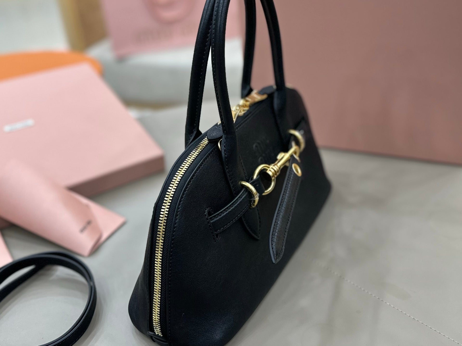 MiuMiu dark navy leather handbag shown from side with zip top and gold-tone rings