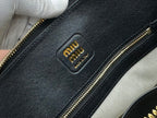MiuMiu dark navy leather bag close-up with embossed logo patch and gold-tone zipper