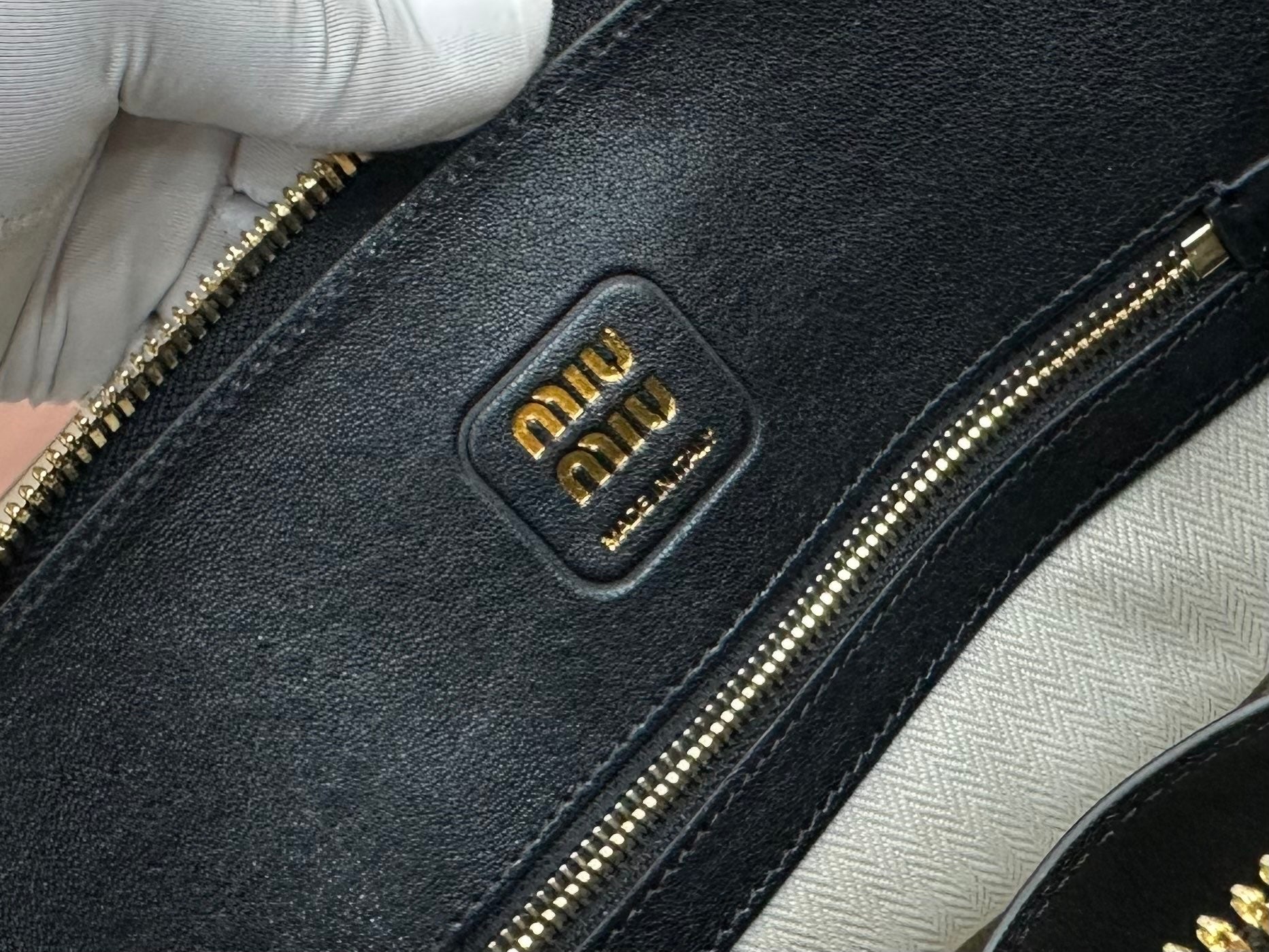 MiuMiu dark navy leather bag close-up with embossed logo patch and gold-tone zipper