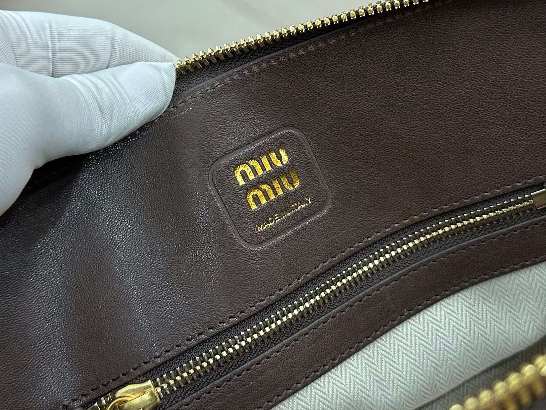 Dark leather logo patch on zip-top bag with gold zipper trim