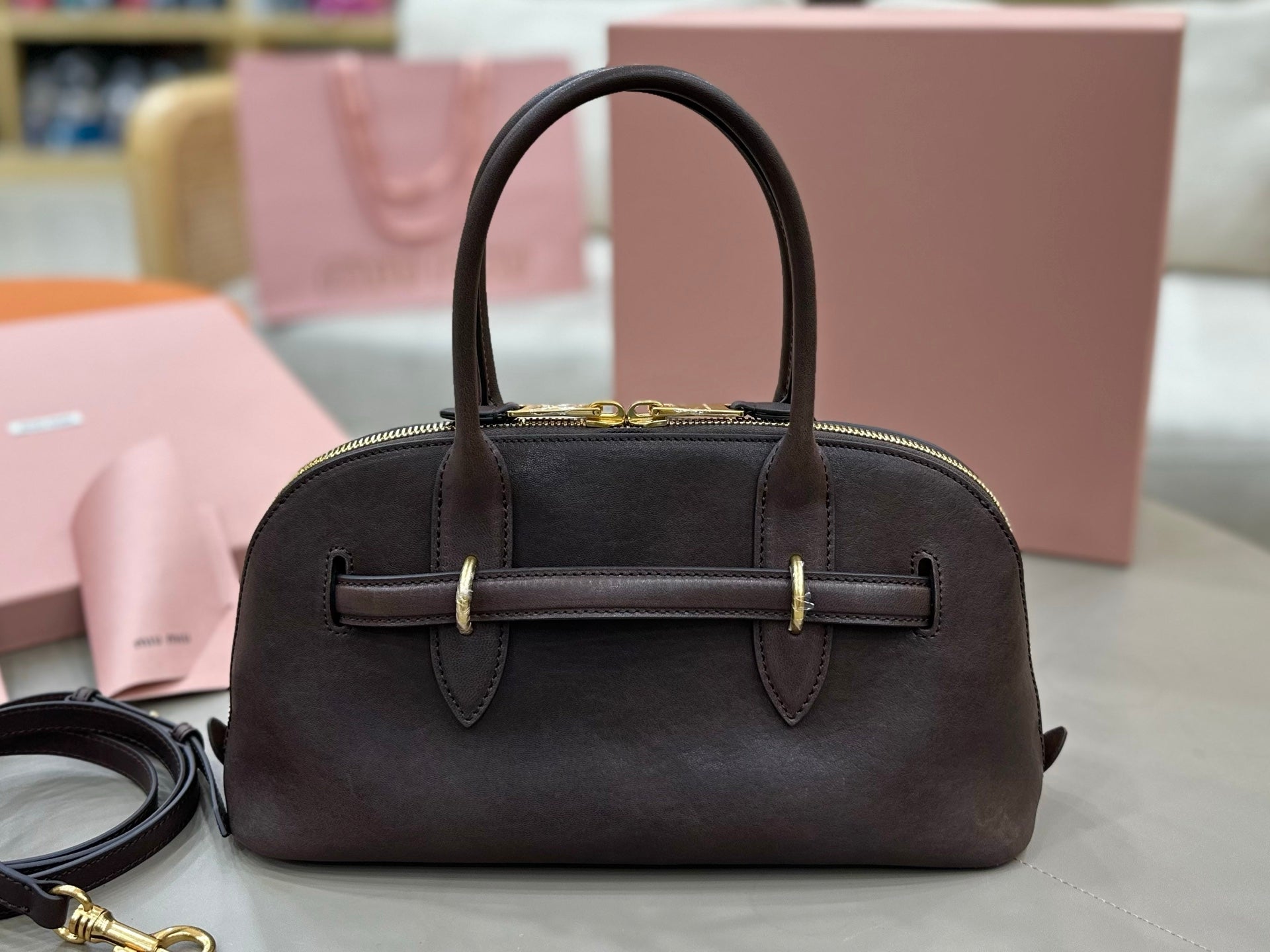 Dark leather dome top-handle bag with front strap detail and gold-tone hardware