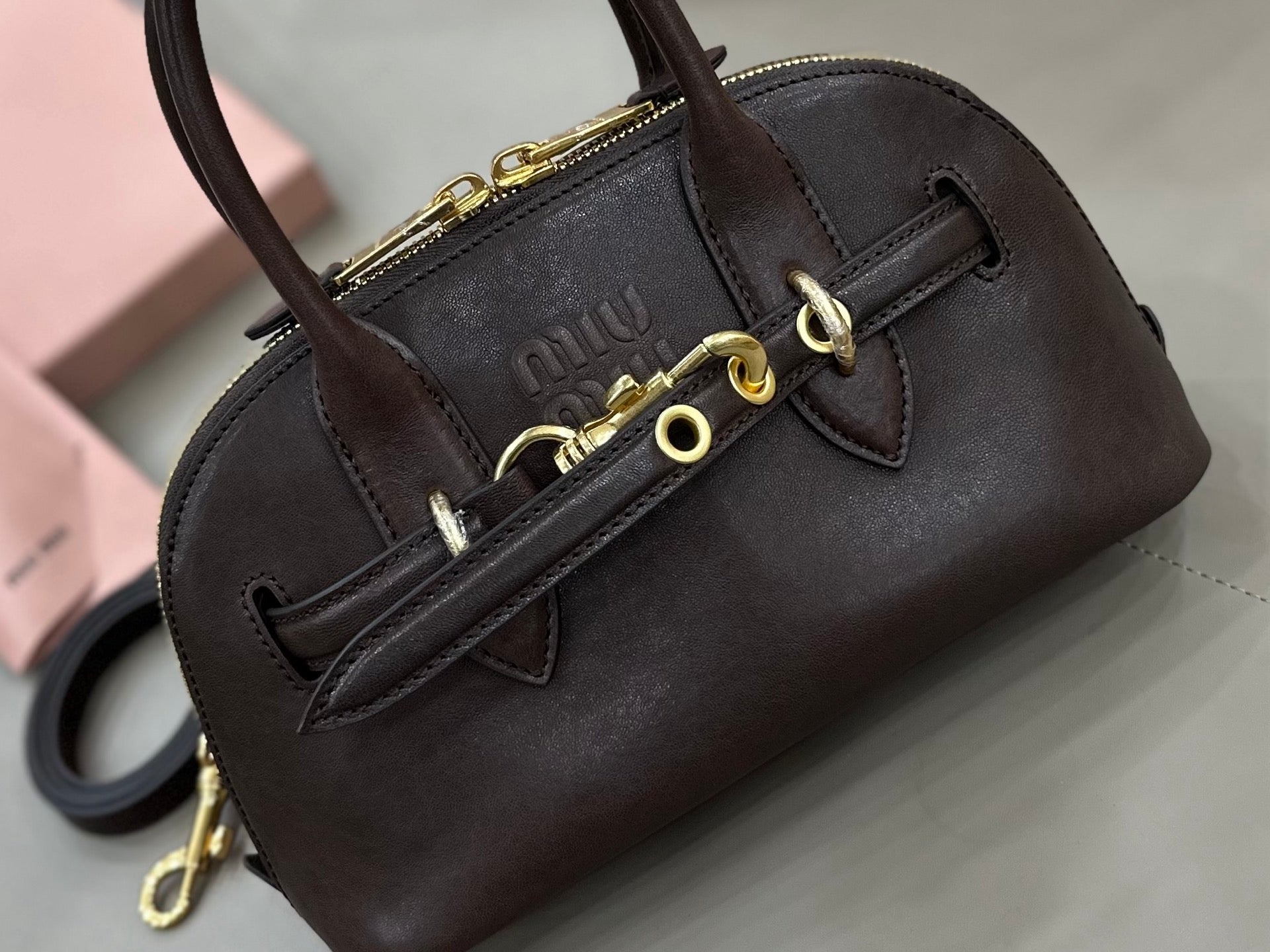 MiuMiu handbag close-up with front strap, gold rings, and zipper, dark brown
