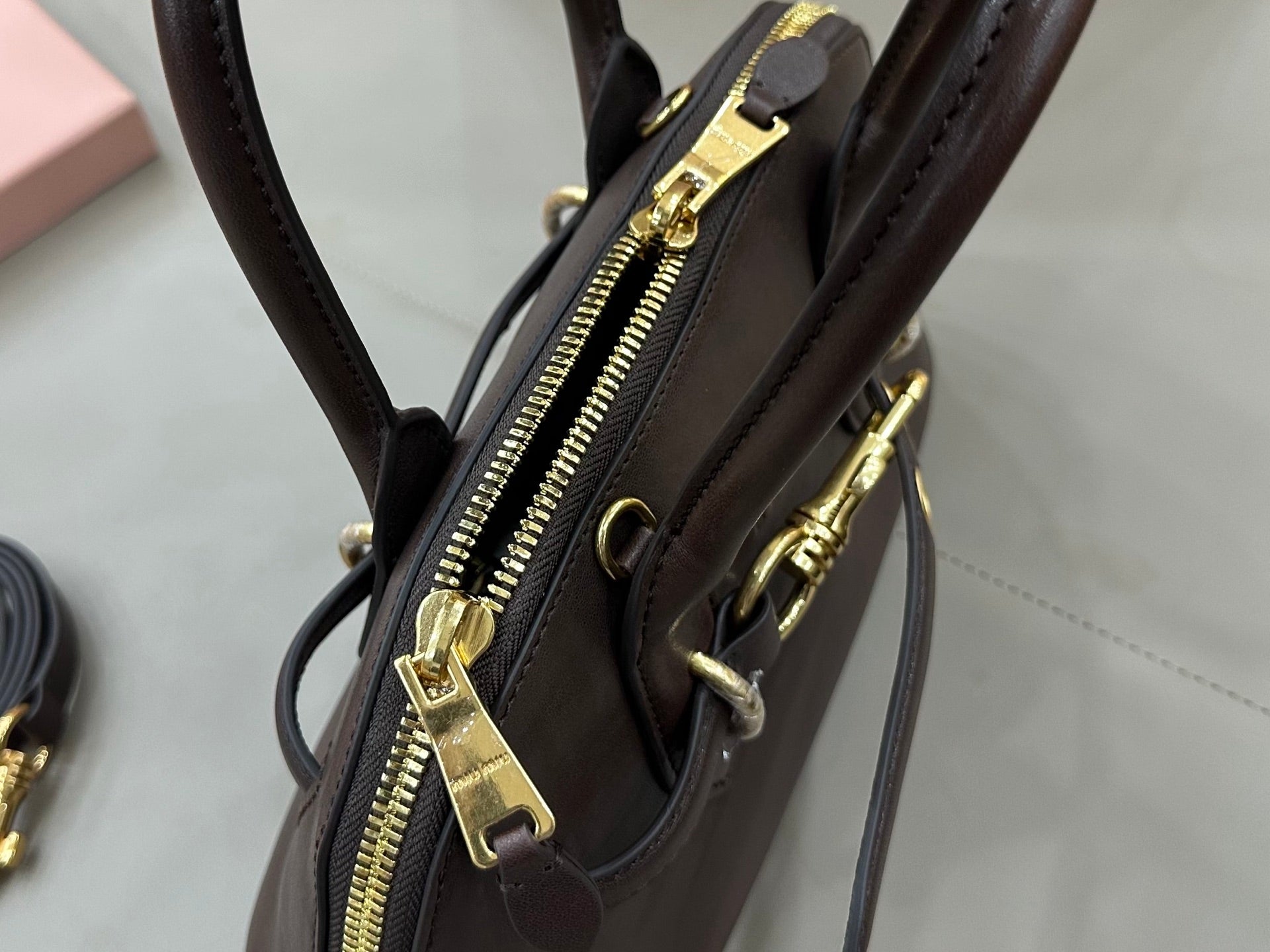 MiuMiu handbag close-up with zipper pull and gold-tone hardware, dark brown