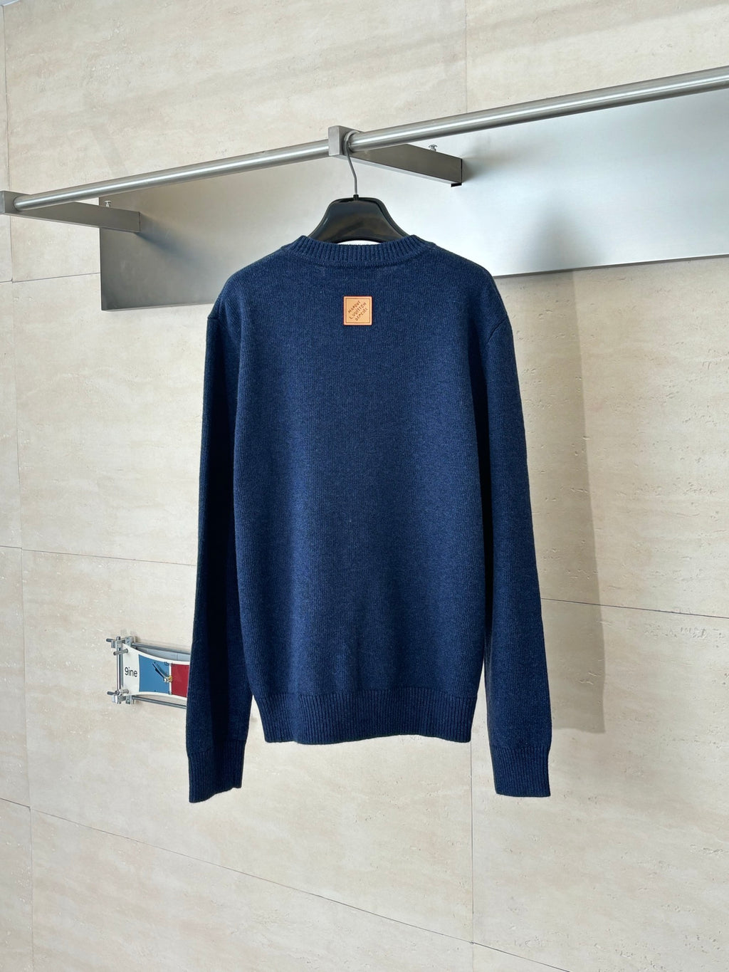 Back of navy knit sweater with small square logo patch at upper back