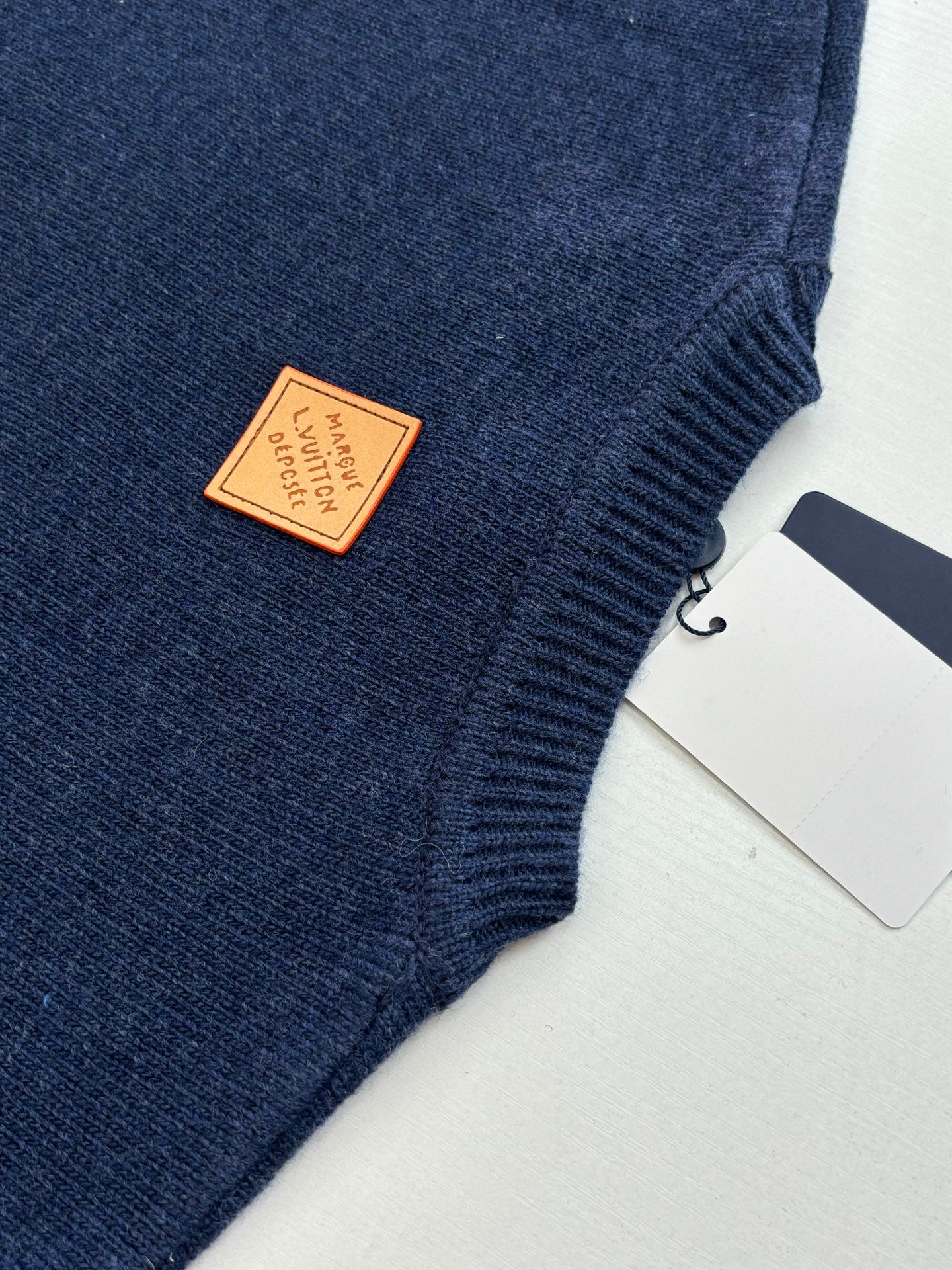 Navy knit sweater with tan brand label patch near side seam and small tag