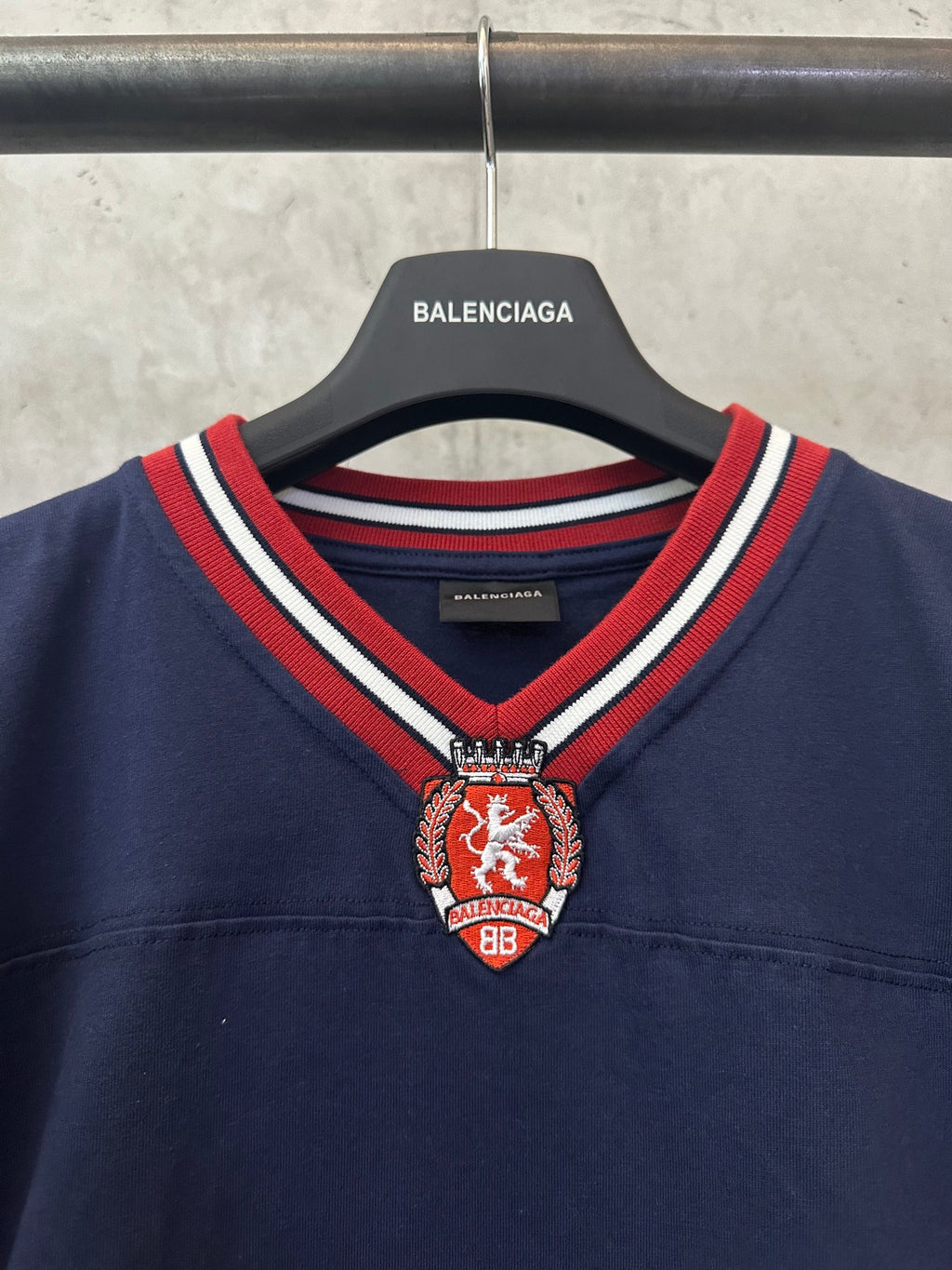 Navy short-sleeve polo shirt with striped V-neck trim and crest badge detail
