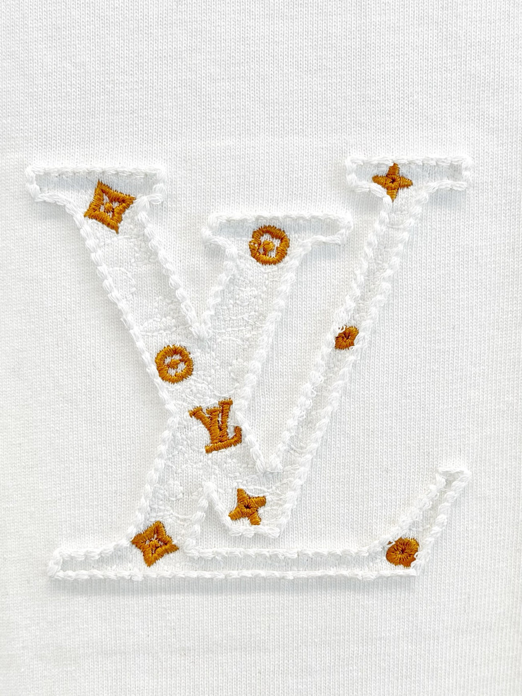 White fabric with V-shaped embroidered logo and small gold emblem details