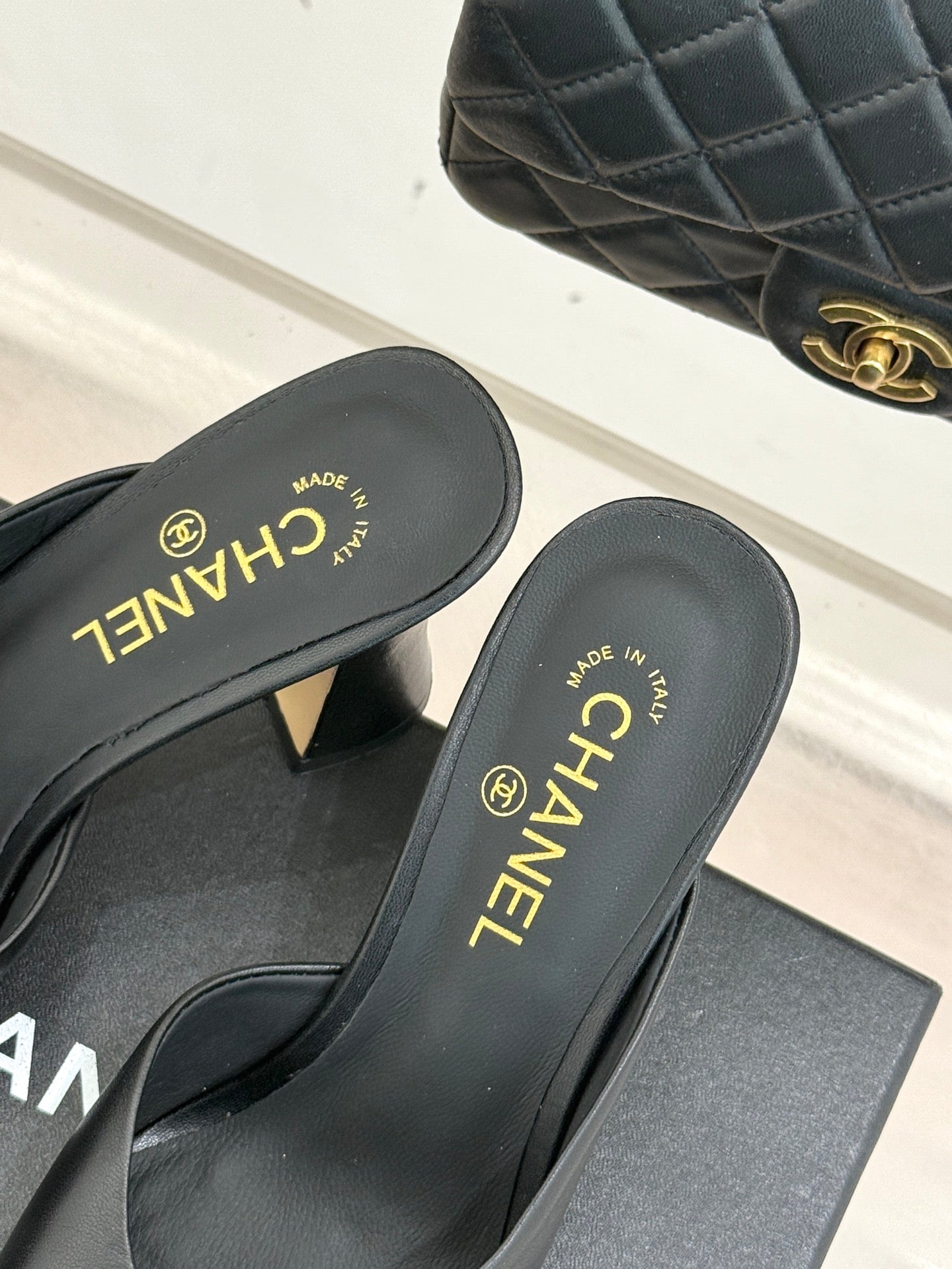 Black Chanel mules close-up showing gold CHANEL branding on insoles