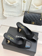 Black heeled slide mules with gold Chanel logo on footbed and glossy toe inserts