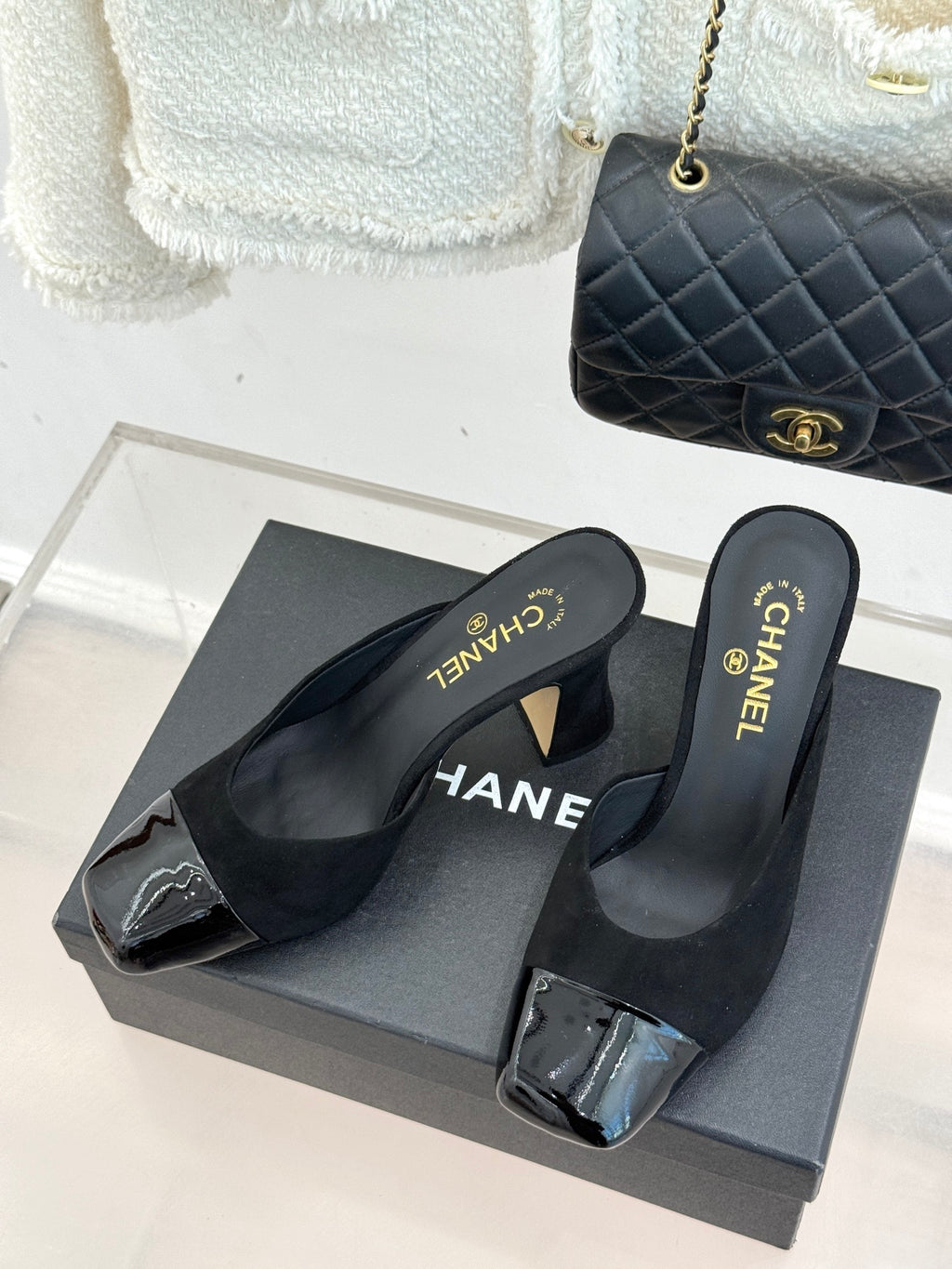Pair of black heeled mule sandals on a box with Chanel logo on the insoles