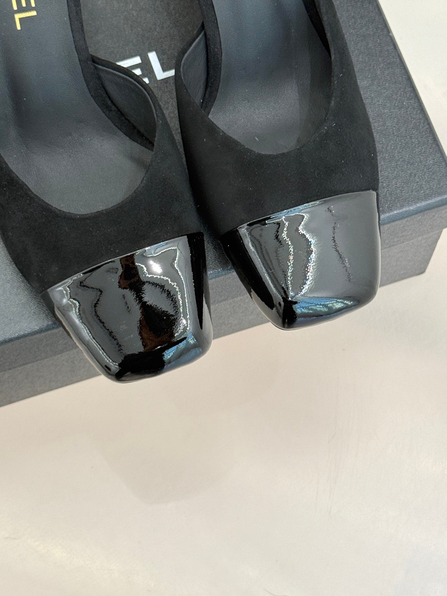 Close-up of black heeled mule sandals with silver patent-style toe caps