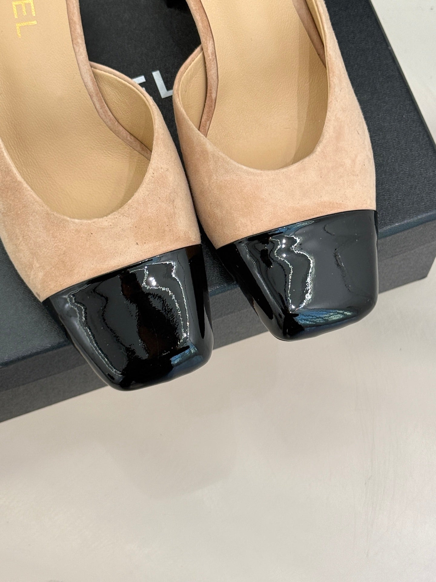 Close-up of beige suede mules with black patent toe panels and block heels