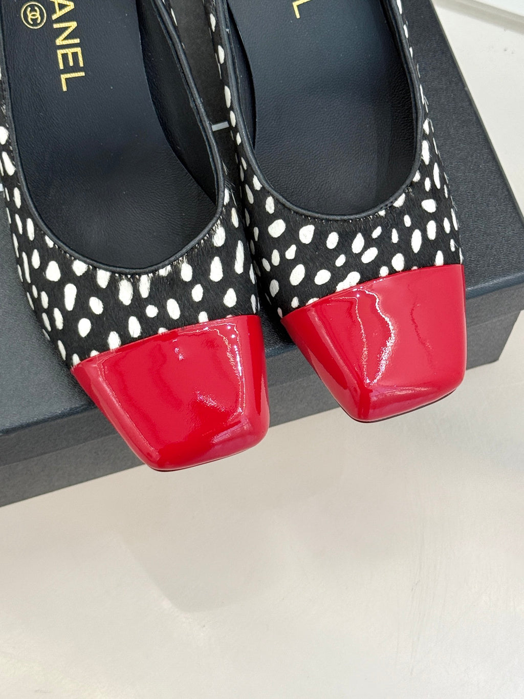 Polka-dot black pumps with red glossy toe cap, close-up front view.