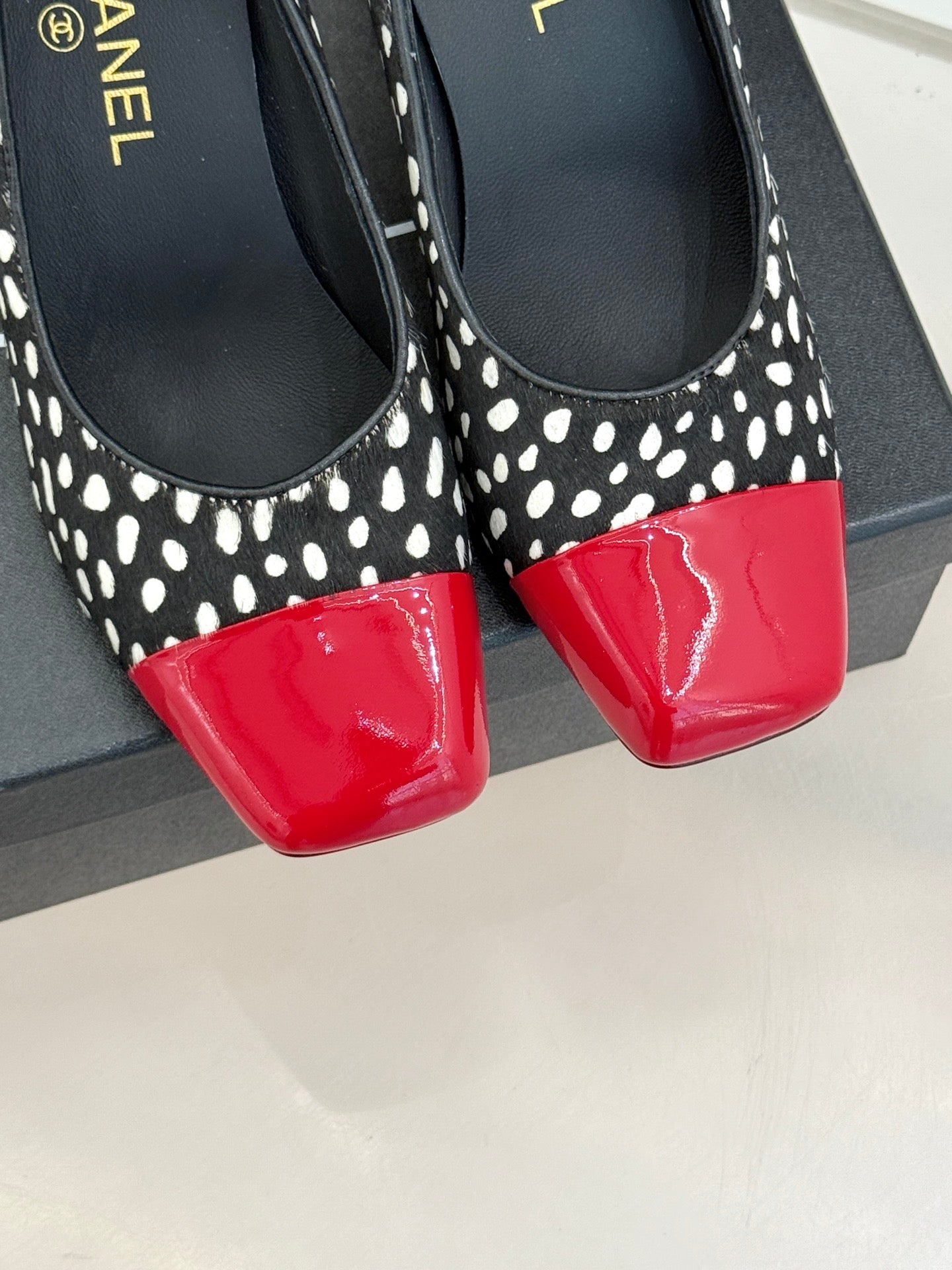 Polka-dot black pumps with red glossy toe cap, close-up front view.