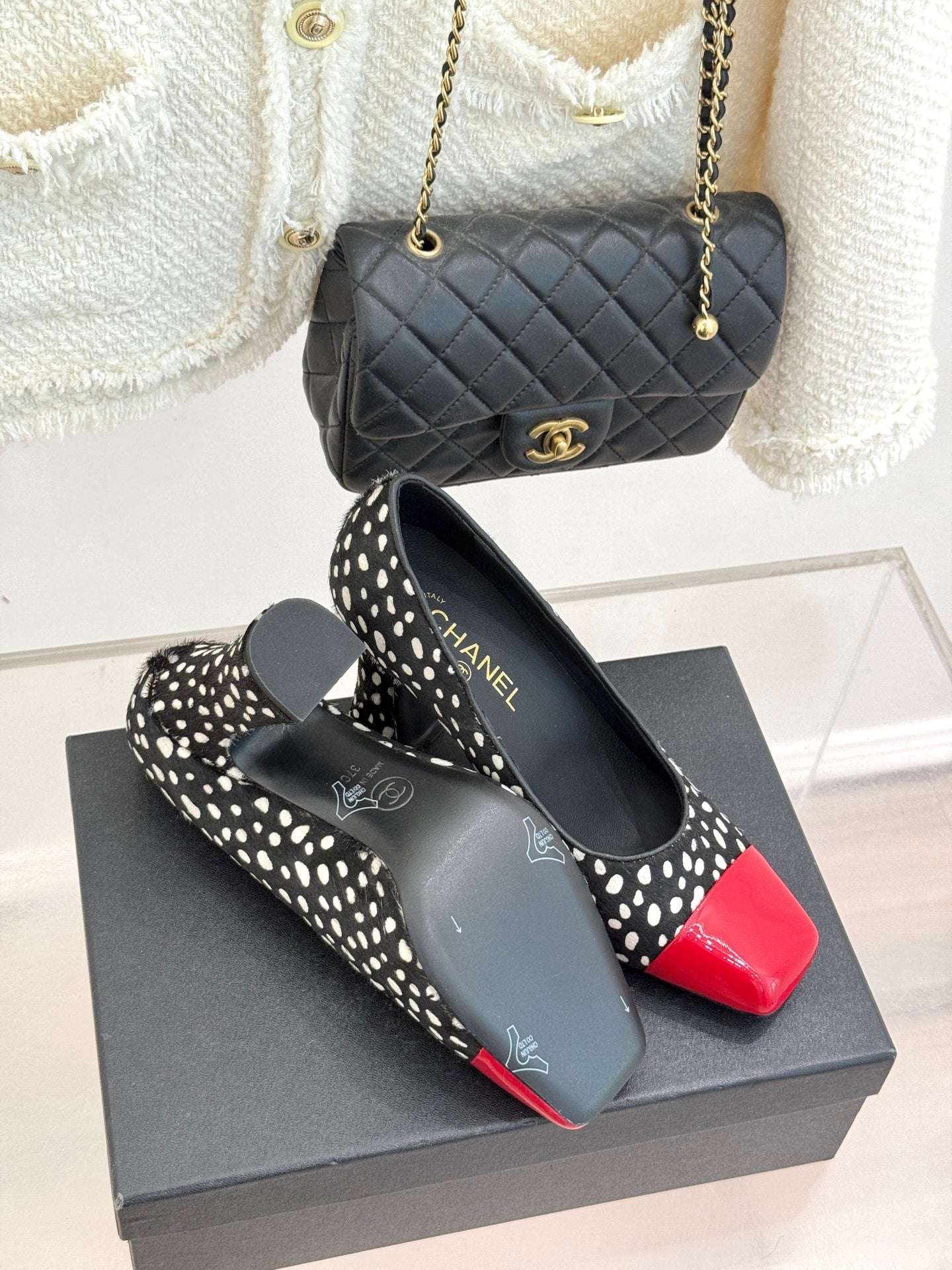 Polka-dot black pumps with red glossy toe cap on black shoebox, angled view.