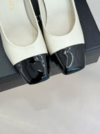 Close-up of white heeled shoes with glossy black toe panels