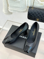 Black heeled pumps with glossy patent toe and Chanel logo on insoles, on box