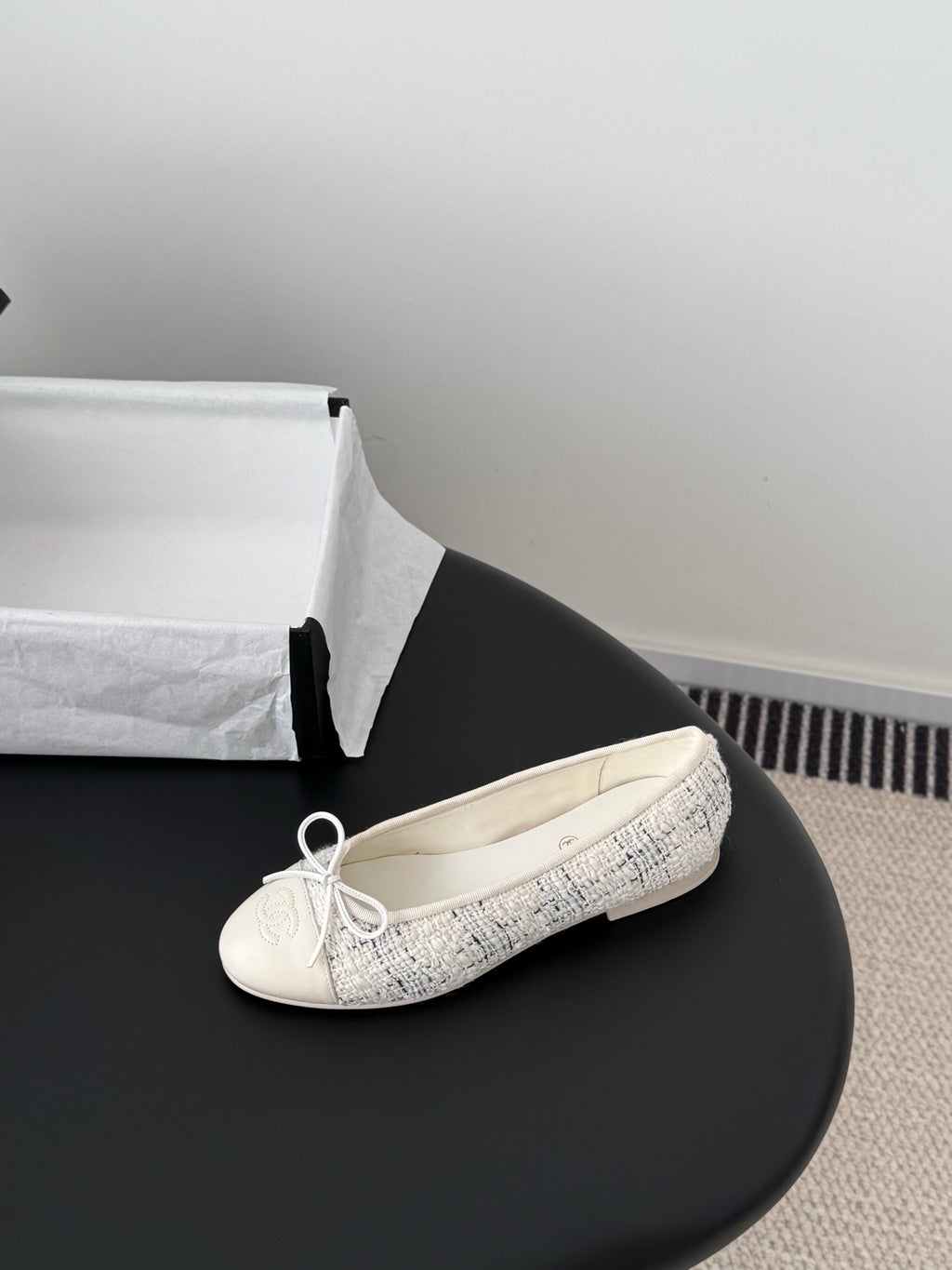 Cream tweed ballet flat with lace-up bow, single shoe on black surface
