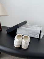 Cream tweed ballet shoes with bow ties, heels-up view on shoe box