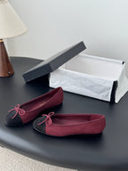 Chanel ballet flats in burgundy with black toe cap and pink bow, shown with shoe box