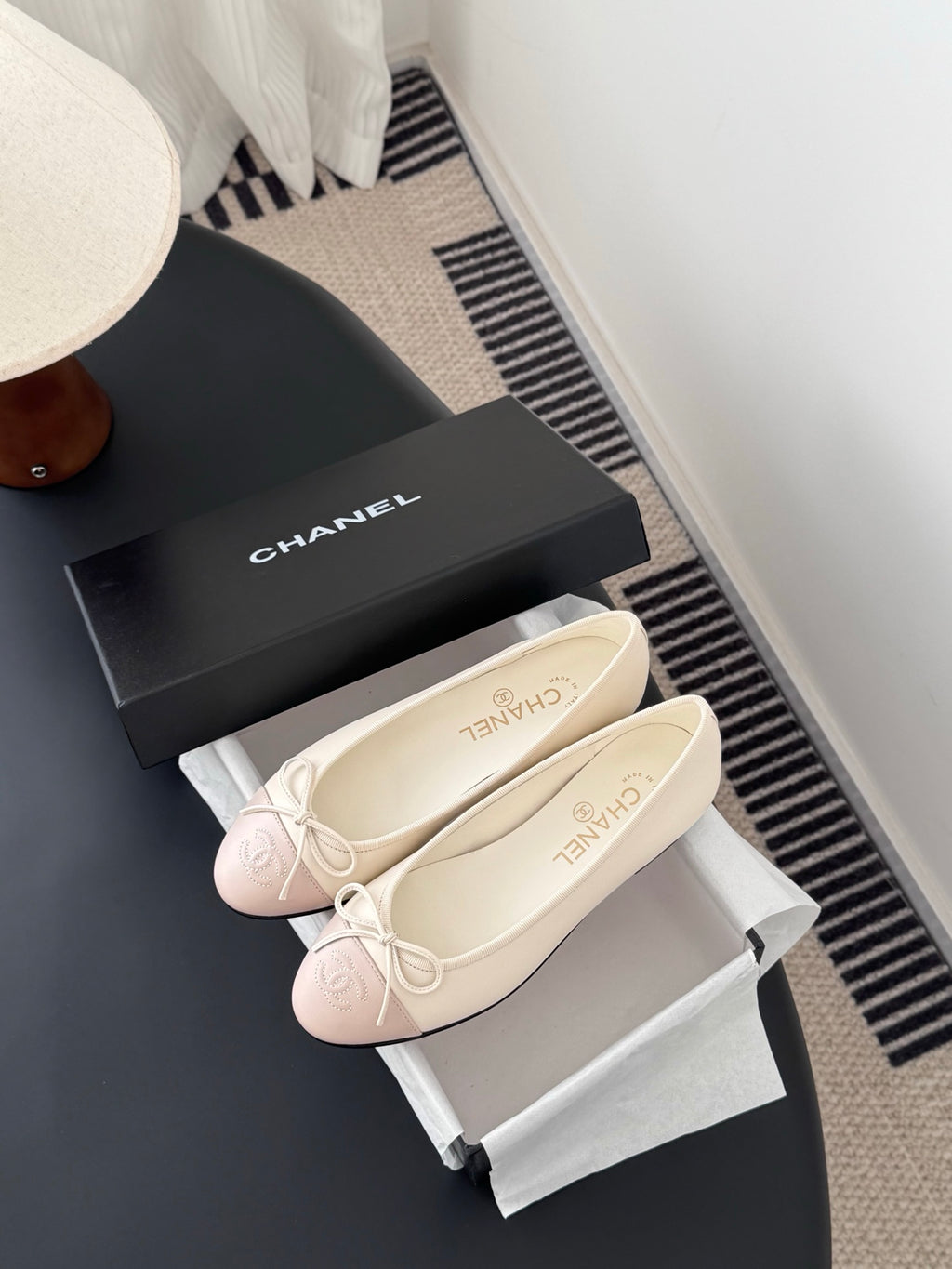 Pale pink ballet flats with white bow laces, placed on white shoe boxes.