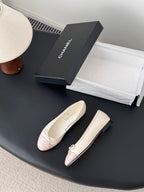 Pair of ballet flats with pale pink toe panels and white bow laces, angled view.