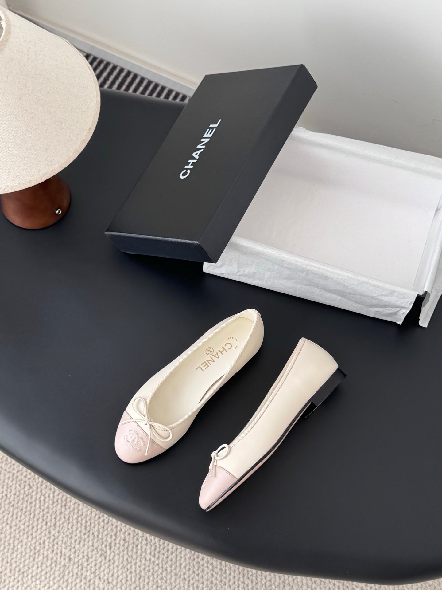 Pair of ballet flats with pale pink toe panels and white bow laces, angled view.