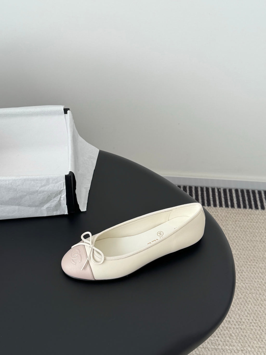 Single pale pink ballet flat with white laces and bow, shown on its side.