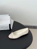 Single pale pink ballet flat with white laces and bow, shown on its side.