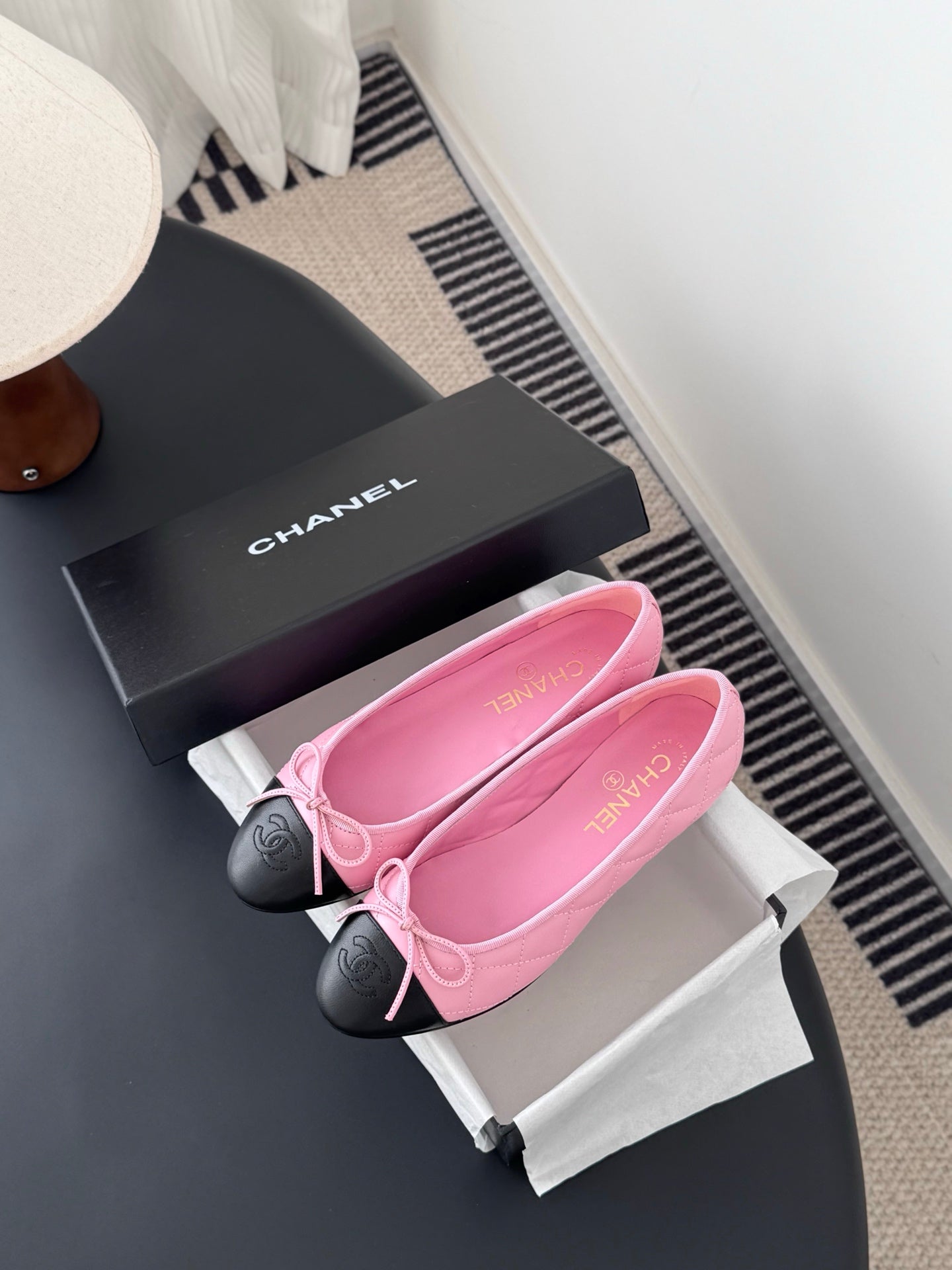 Chanel pink ballet flats with bow and black toe caps next to black logo box