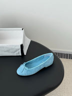 Light blue Chanel ballet flats on black surface, side view with bow at toe