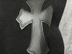 Black sweater with silver cross-stitch applique detail on front shoulder.
