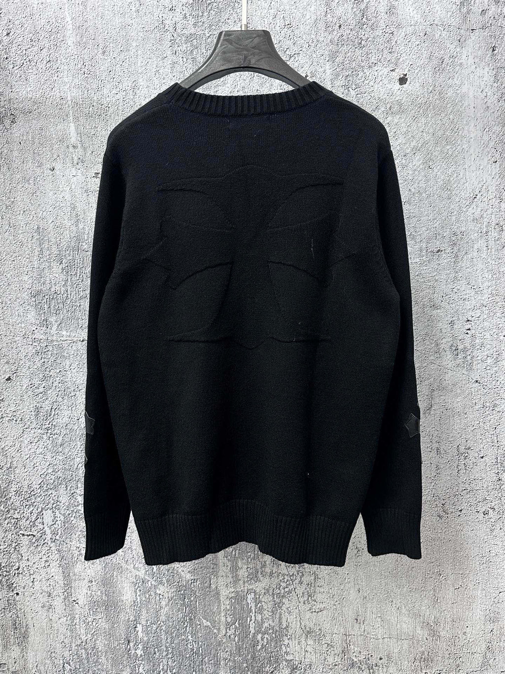 Black long-sleeve knit sweater with ribbed crew neck and stitched back detail.
