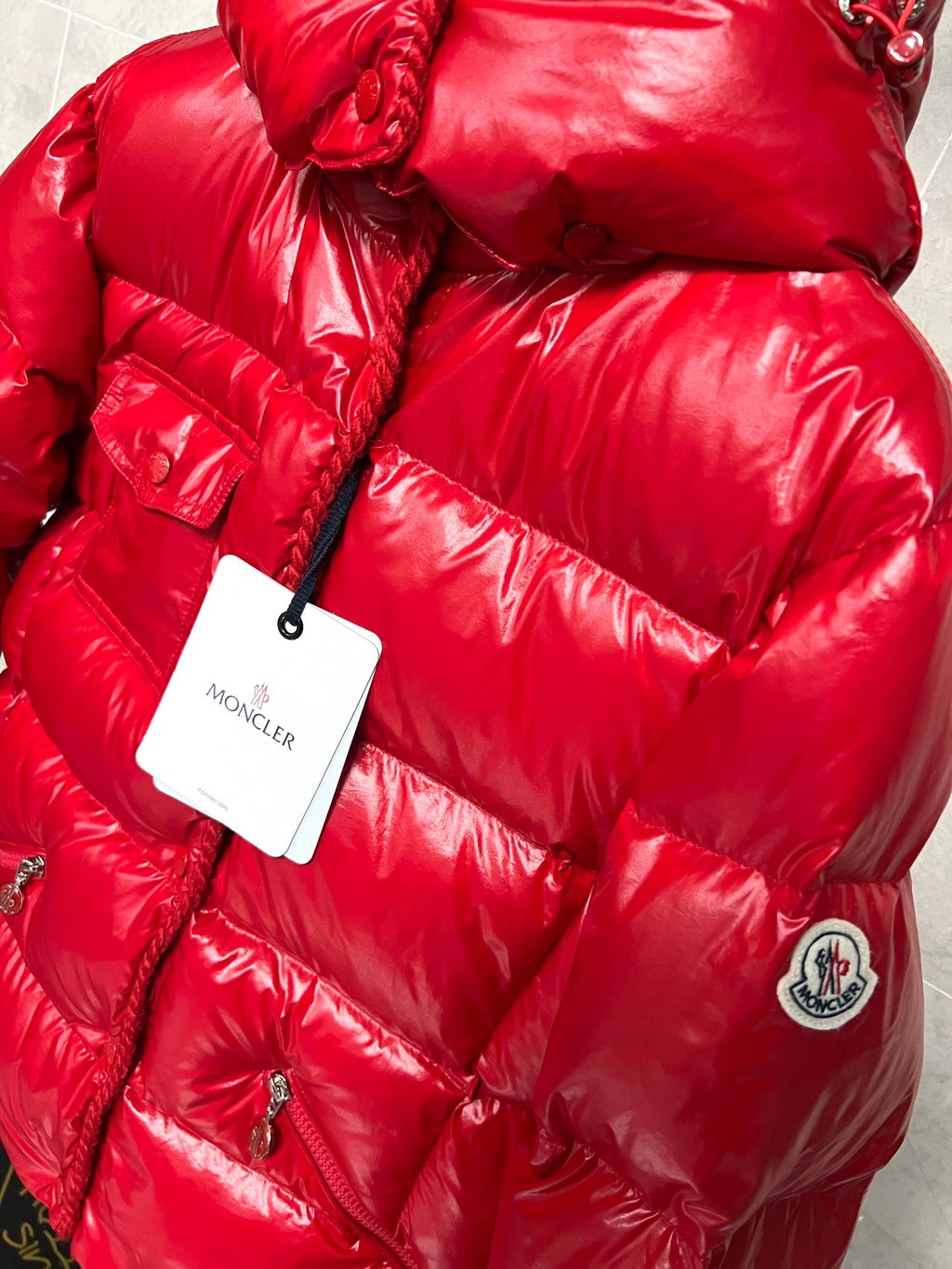 Moncler long red puffer jacket close-up with hood drawstring, quilted texture and logo patch