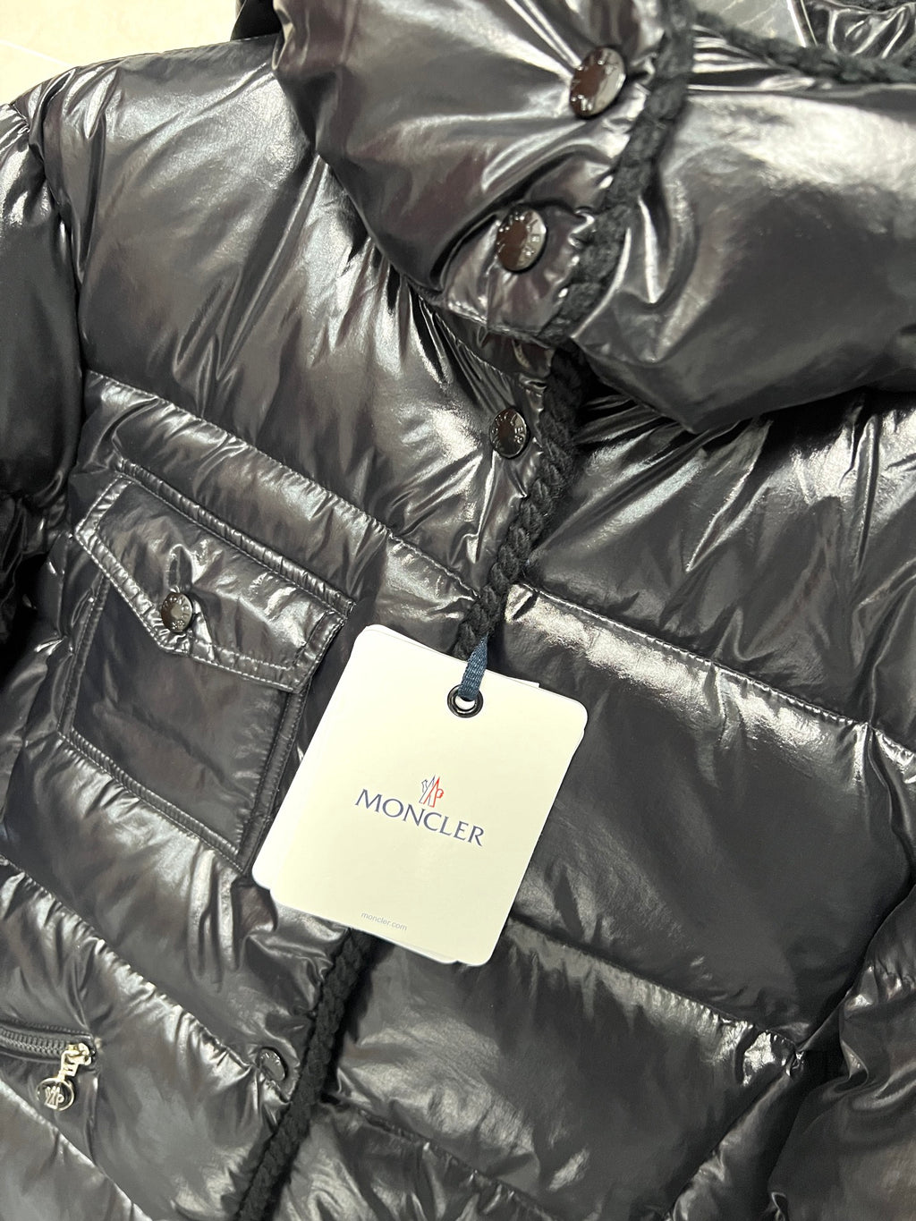 Moncler long puffer jacket chest detail, glossy black with emblem patch and hanging tag