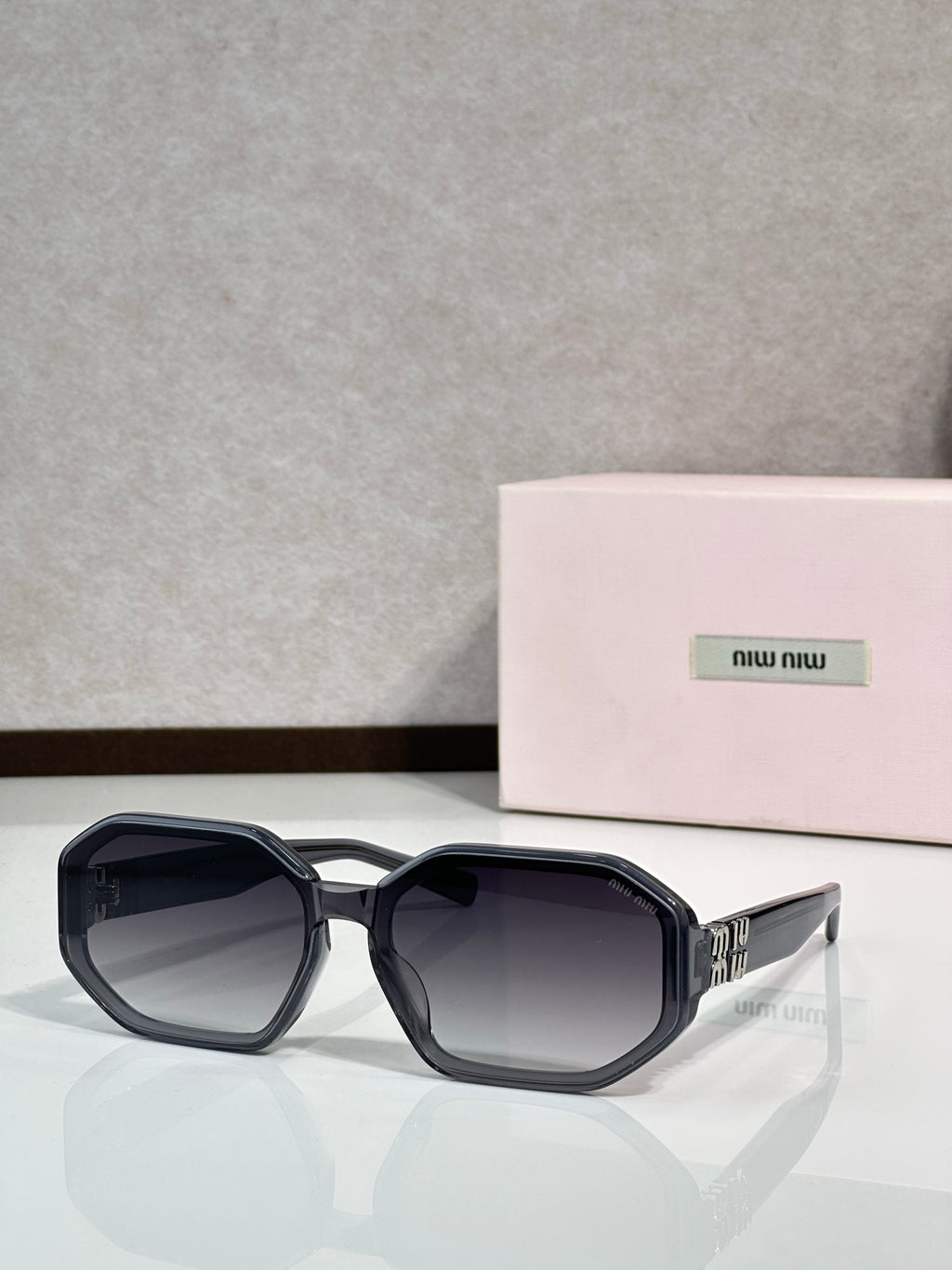 Square sunglasses with navy-dark tinted lenses and black frame, featuring Miu Miu logo.