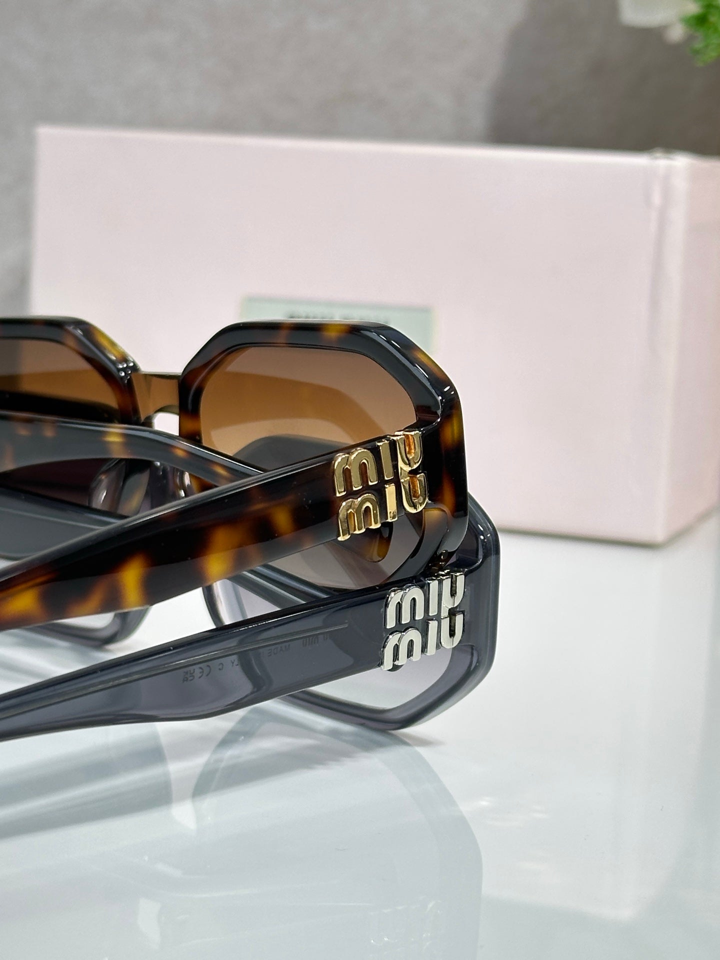 Tortoise sunglasses close-up: Miu Miu logo on temple with dark lens edge visible.