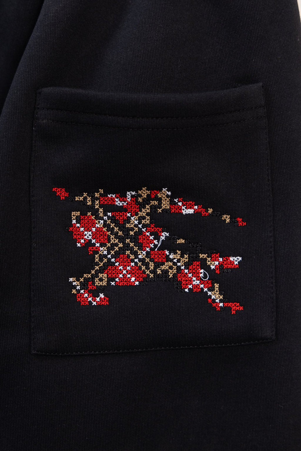 Black pants with embroidered red-and-gold emblem patch on side pocket