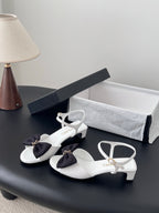 Chanel bow sandals in white with black knot detail and low heel, ankle strap